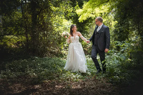 Ein Hochzeitspaar hält sich auf einem Waldweg an den Händen